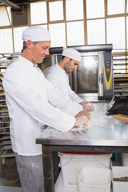istock Focused bakers kneading dough at counter 467825526