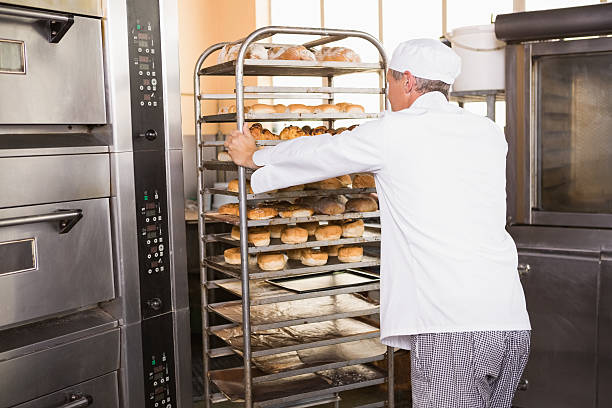 istock Smiling baker pushing tray of bread 467825832