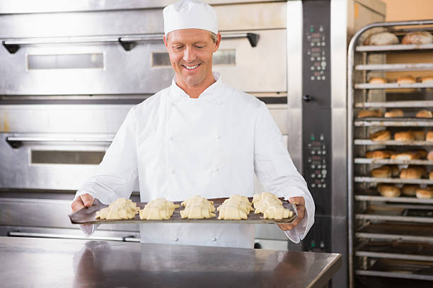 istock Smiling baker holding tray of raw dough 467826178