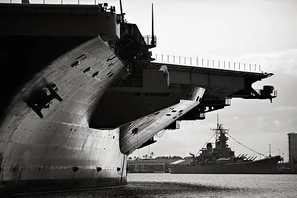 This black and white photo depicts the battleship USS Missouri in the shadow of the USS Ronald Reagan aircraft carrier in Pearl Harbor.