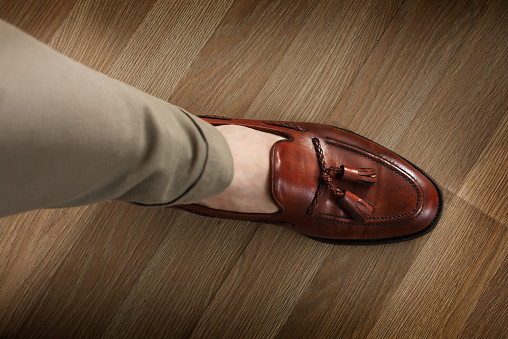 Sockless male leg in tasseled loafer, dark leaf colored and burnished. Preppy style dressed man wearing cushioned pants and loafers