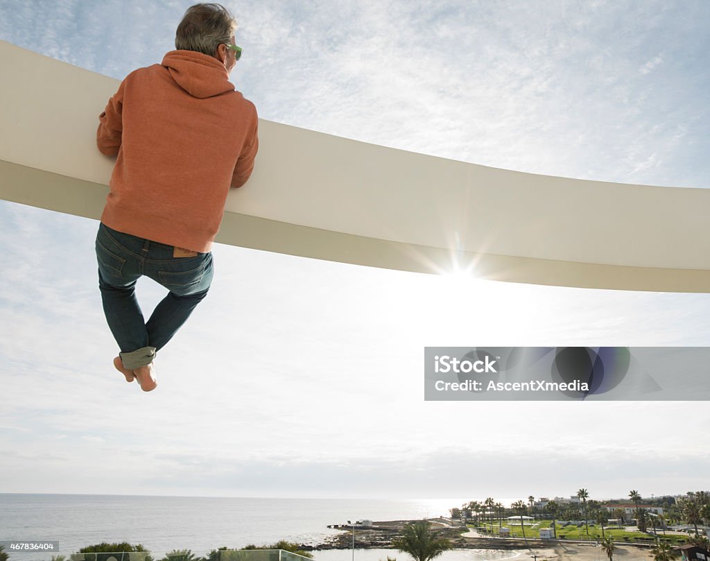 Man pulls himself up onto beam above coastline, sea Hanging Stock Photo
