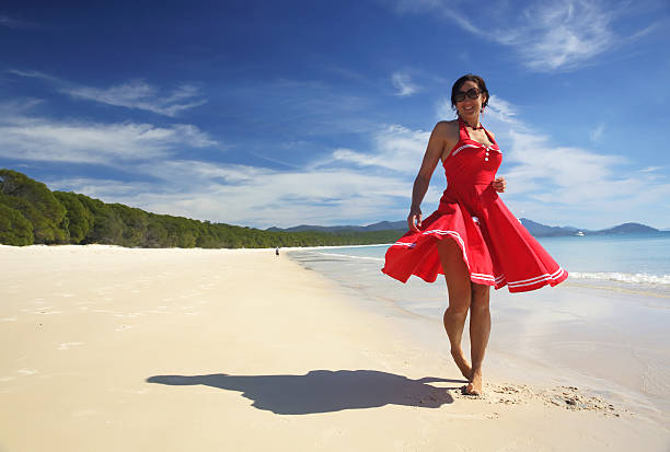 Beautiful woman in bright red dress dances with happiness on Whitehaven Beach in the Whitsunday Islands of the Great Barrier Reef, Australia