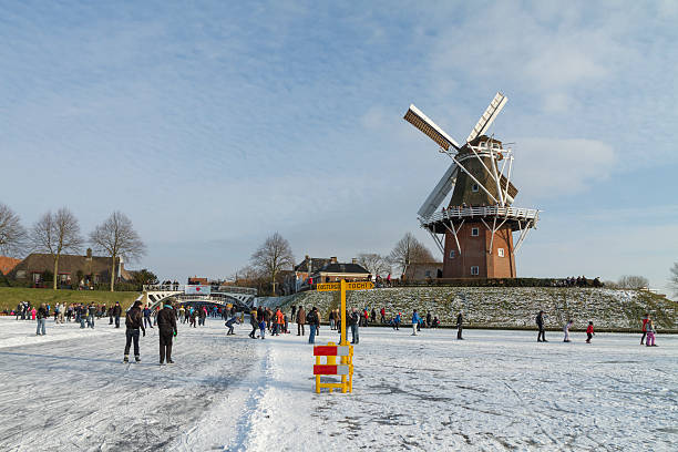 Skaters on frozen canals in Dokkum,  Friesland, with old windmil Dokkum, the Netherlands - February 11, 2012: Skaters on frozen canals in Dokkum,  Friesland, the Netherlands with old windmill called "Zeldenrust" on top of the rampart and skating sign post on the canal. friesland netherlands stock pictures, royalty-free photos & images