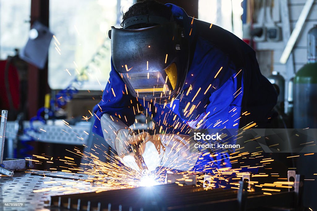 Welder welding metal in workshop with sparks Welder bonding metal with welding device in workshop, lots of sparks to be seen, he wears welding goggles Welder Stock Photo