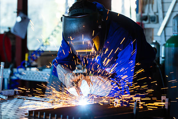 Welder welding metal in workshop with sparks Welder bonding metal with welding device in workshop, lots of sparks to be seen, he wears welding goggles metalwork stock pictures, royalty-free photos & images