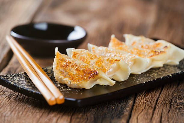 Japanese Food Gyoza A plate of authentic Japanese gyoza potsticker appetizers with dipping sauce and chopsticks, against a wooden background. chinese dumpling photos stock pictures, royalty-free photos & images