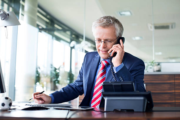 Businessman answering a phone call Mature businessman working at his desk answering a phone call landline phone stock pictures, royalty-free photos & images
