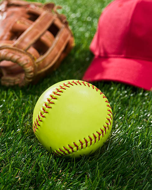 istock Yellow Softball in the grass with glove and red hat 467870606