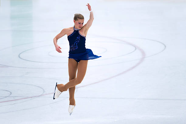 weibliche skater performing springen während figure skating competition - eiskunstlauf stock-fotos und bilder