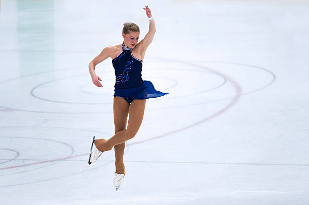 Female Skater Performing Jump During Figure Skating Competition Front view of young adult women performing jump on the indoor rink figure skating stock pictures, royalty-free photos & images