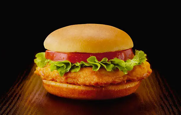 Chicken burger with lettuce and tomato slice in white bread bun. Placed on dark reflective surface and in black background.