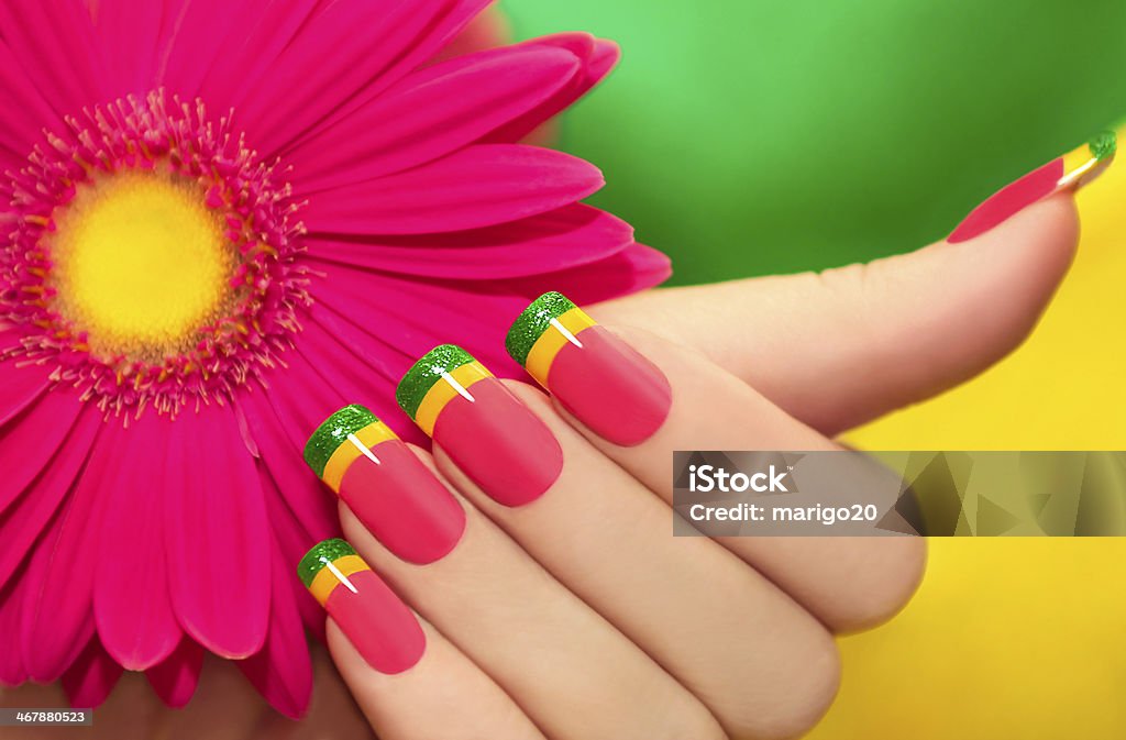 Multicolored manicure. Multicolored manicure with pink,yellow and green lacquer against the background with gerberas. Beautiful People Stock Photo