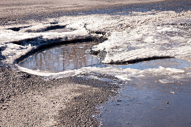 istock Very large pothole with water and ice in the road 467882140