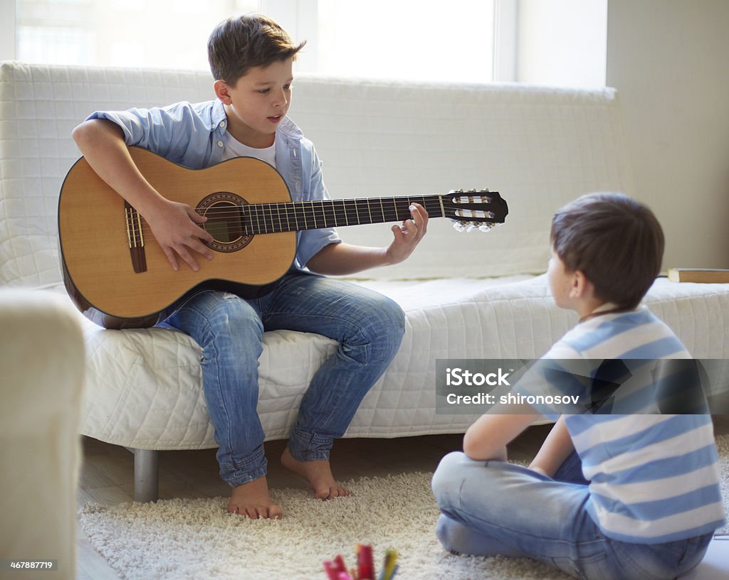 Learning how to play the guitar Portrait of handsome boy playing the guitar with his brother near by Brother Stock Photo