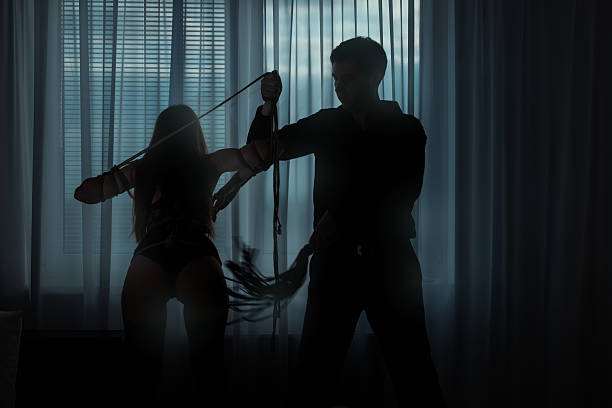 Woman bound and beaten man.  Only visible silhouettes of men and women. Man beats a woman whip in a dark room. Woman connectivity ropes. whip tortured punishment cruel stock pictures, royalty-free photos & images