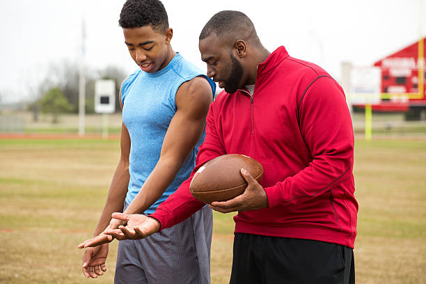 Coach training a high school athlete for football. Coach giving tips to an athlete on football techniques. coach stock pictures, royalty-free photos & images