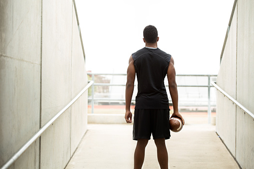 Rear view of an African American teenager holding a football.