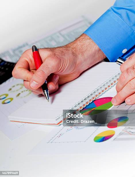 Caucasian Businessman Writing Report In Notepad And Analyzing Financial Figures Stock Photo - Download Image Now