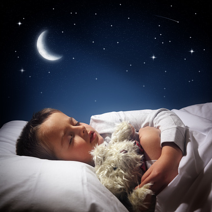 Child sleeping and dreaming in his bed under the moon, stars and blue moonlit night sky