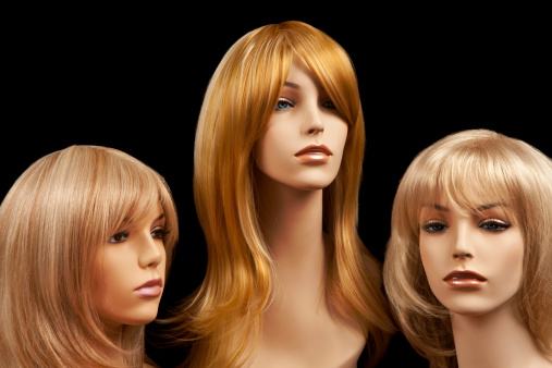 Three blond mannequin heads with wigs on black background.