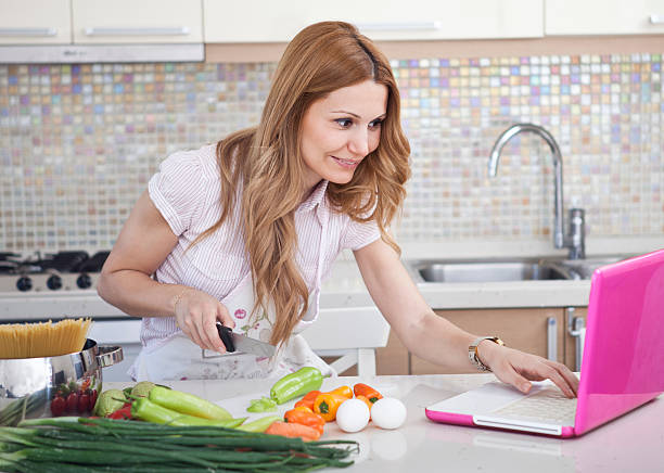 istock female cooking and looking at laptop in kitchen 467905375