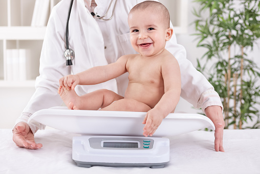 Happy smiling baby child in pedrician office, measuring weight