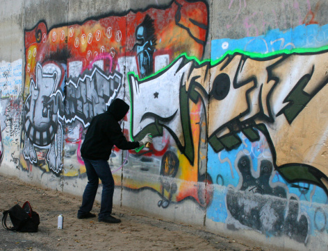 One male, unrecognizable male artist painting a graffiti on the wall.