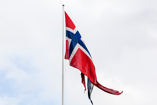 Norwegian state and war  flag in red white and blue waving in the breeze  towards alight clouded sky.