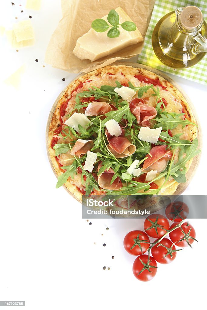 Preparing a gourmet Italian pizza Preparing a gourmet Italian pizza with delicious thinly sliced prosciutto ham, cherry tomatoes , cheese, oil and fresh herbs including rocket and basil Arugula Stock Photo