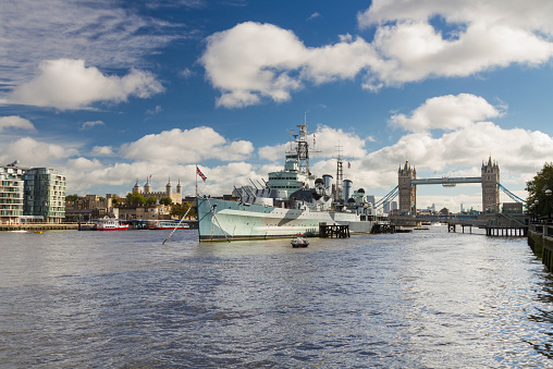 The warship turned museum HMS Belfast on the river Thames on a cloudy autumn day, with the Tower of London and Tower Bridge in the background.