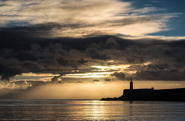 istock Sunrise sky over calm water ocean with lighthouse and harbor 467929251