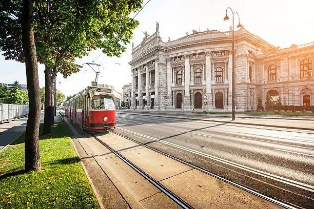 Beautiful view of famous Wiener Ringstrasse with historic Burgtheater (Imperial Court Theatre) and traditional red electric tram at sunset in Vienna, Austria.