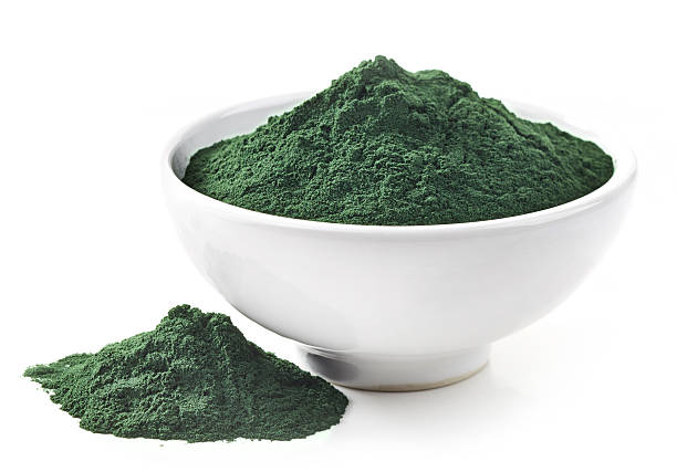 White bowl of green spirulina algae powder spilling out bowl of spirulina algae powder isolated on white spirulina stock pictures, royalty-free photos & images