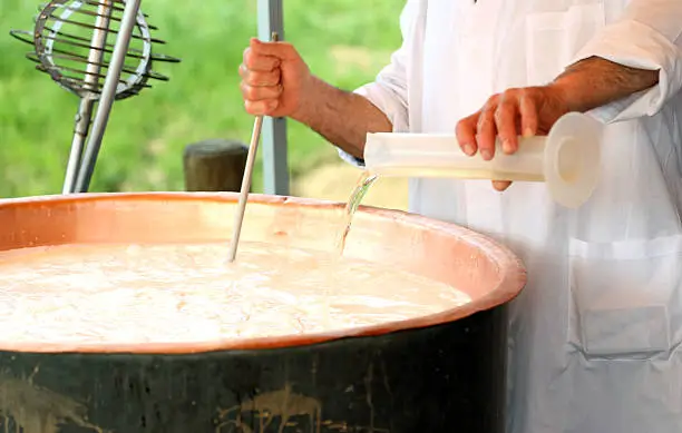 expert Cheesemaker pours milk rennet in copper pot for making cheese in the dairy
