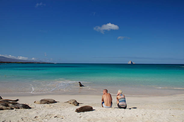 Young couple in the Galapagos sitting on the beach enjoying the sea lions 