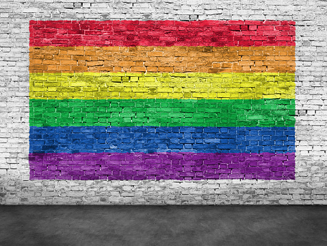 Rainbow flag painted over old white brick wall