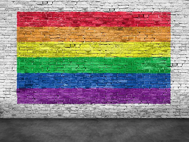 Photo of Rainbow flag painted over white brick wall
