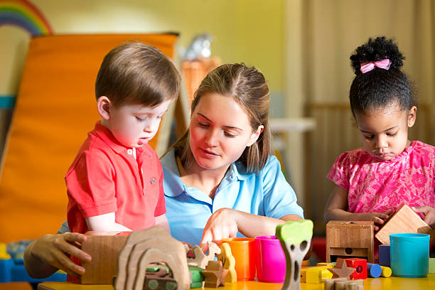 istock Nursery teacher supervising children playing with building blocks 467960262