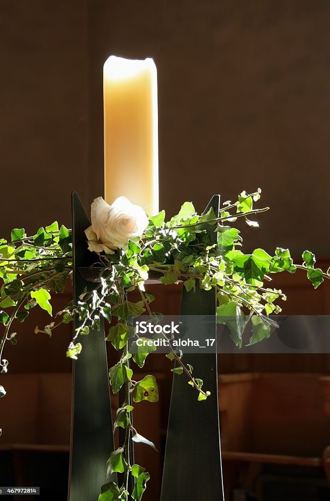 Candle in church A big candle in a church. Decorated with a rose and ivy. The light that touches the candle comes from the church windows. 2015 Stock Photo