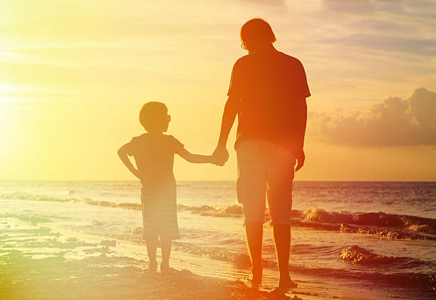 istock Father and son holding hands at the beach at sunset 467985414