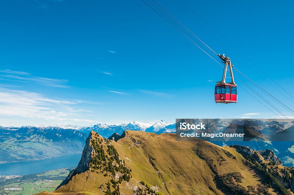 Swiss Alps Cable Car Red cable car on the way to the Stockhorn, Bernese Alps, Switzerland. At the foot of the mountains lake of Thun. Directly below the gondola three famous mountains of the Bernese Alps: Eiger, Mönch and Jungfrau. Among the shadows the north face of Eiger. Overhead Cable Car Stock Photo