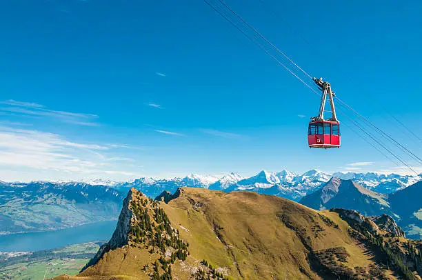 Red cable car on the way to the Stockhorn, Bernese Alps, Switzerland. At the foot of the mountains lake of Thun. Directly below the gondola three famous mountains of the Bernese Alps: Eiger, Mönch and Jungfrau. Among the shadows the north face of Eiger.