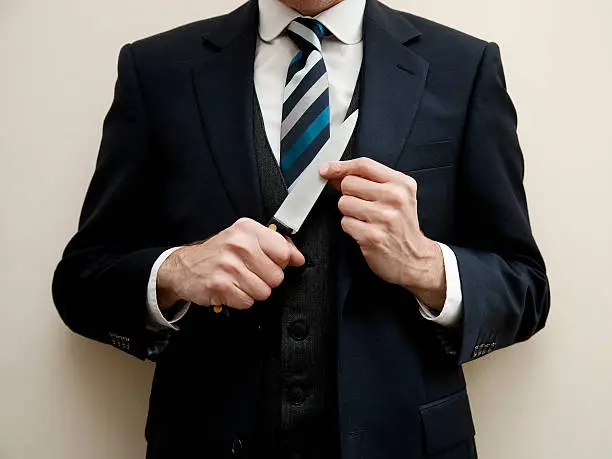 Close up of the mid section of a man in a smart dark suit and stripey neck tie and holding a sharp knife.