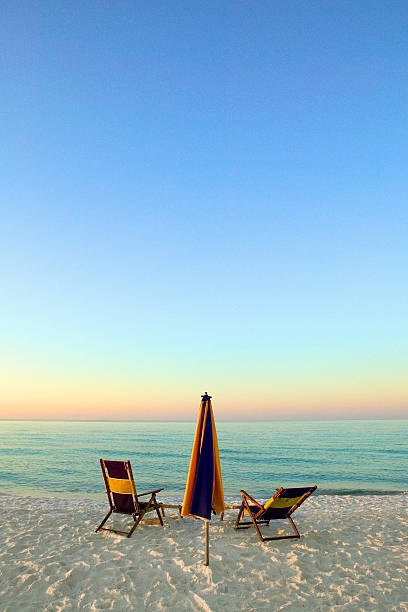 Wooden beach chairs on beach at sunset or sunrise at dusk with lit  candles. Sunhat's hanging on top of chairs. No people. Santa Rosa Beach, Destin, Florida, USA. Gulf of Mexico.