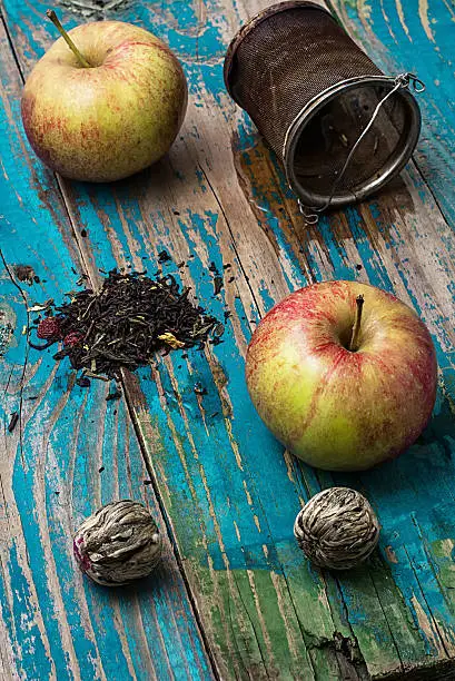 tea leaves and red apple on wooden background.The image is tinted in vintage style