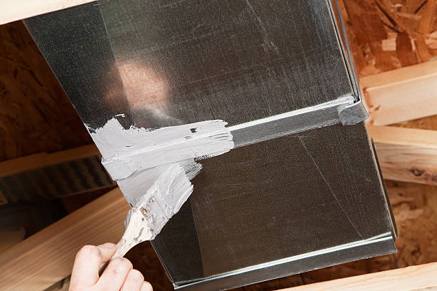 A male hand, holding a paintbrush, is spreading caulk over a house HVAC air duct seam. Caulking ducts prevents air-conditioned or heated air from escaping the duct and prevents ambient air from entering the system. This is a new practice in homebuilding to increase energy efficiency, eventually it may become standard or mandatory.