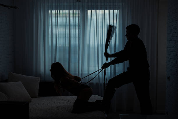 Man beats a woman. Black contours silhouette.  Man beats a woman with a whip in a dark room on the bed. whip tortured punishment cruel stock pictures, royalty-free photos & images