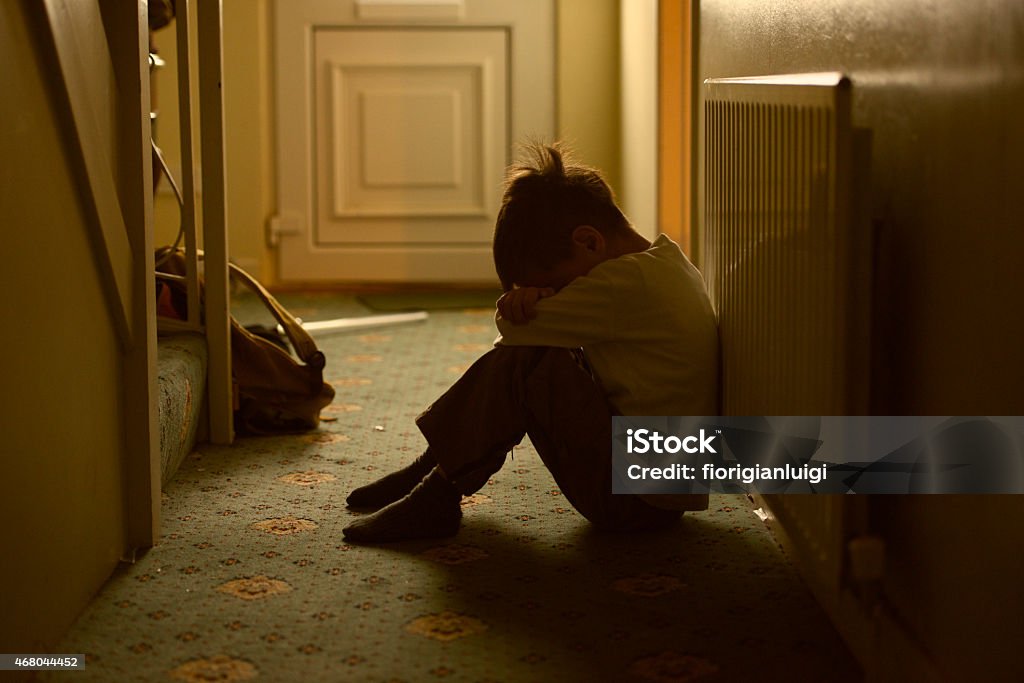 child victim of maltreatment family sad child with his head between his legs left alone at home Child Stock Photo
