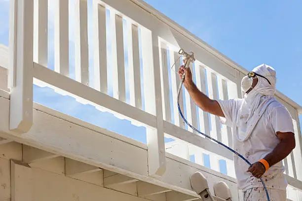 Photo of House Painter Spray Painting A Deck of A Home